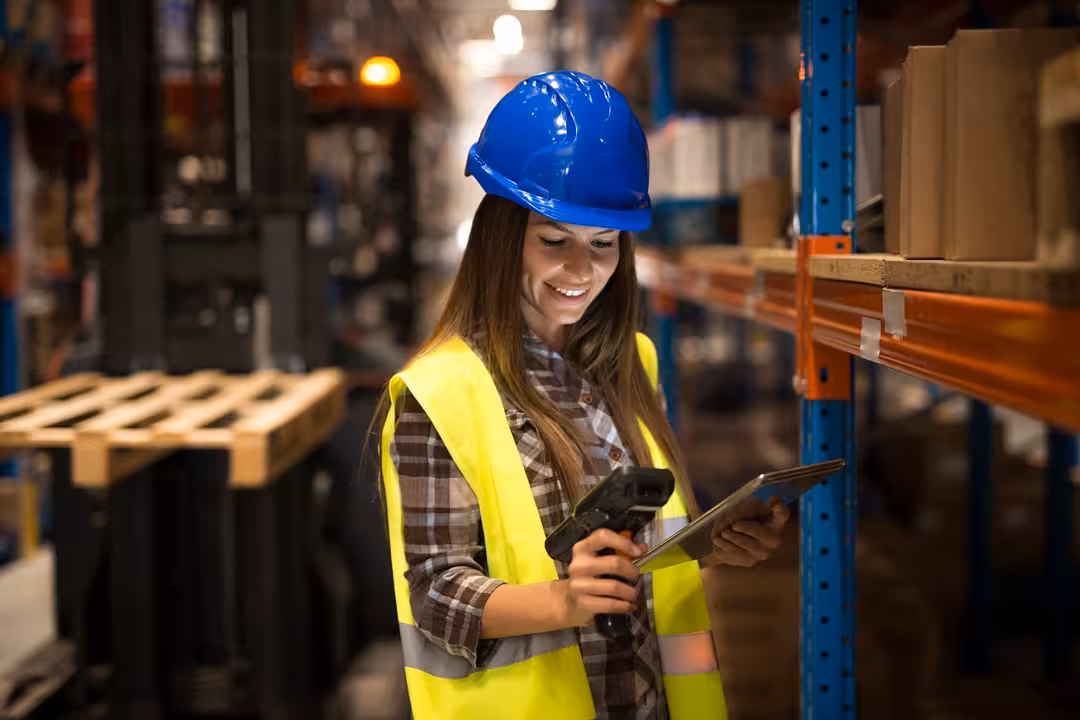 Smiling female worker holding tablet and bar code scanner checking inventory in distribution warehouse.