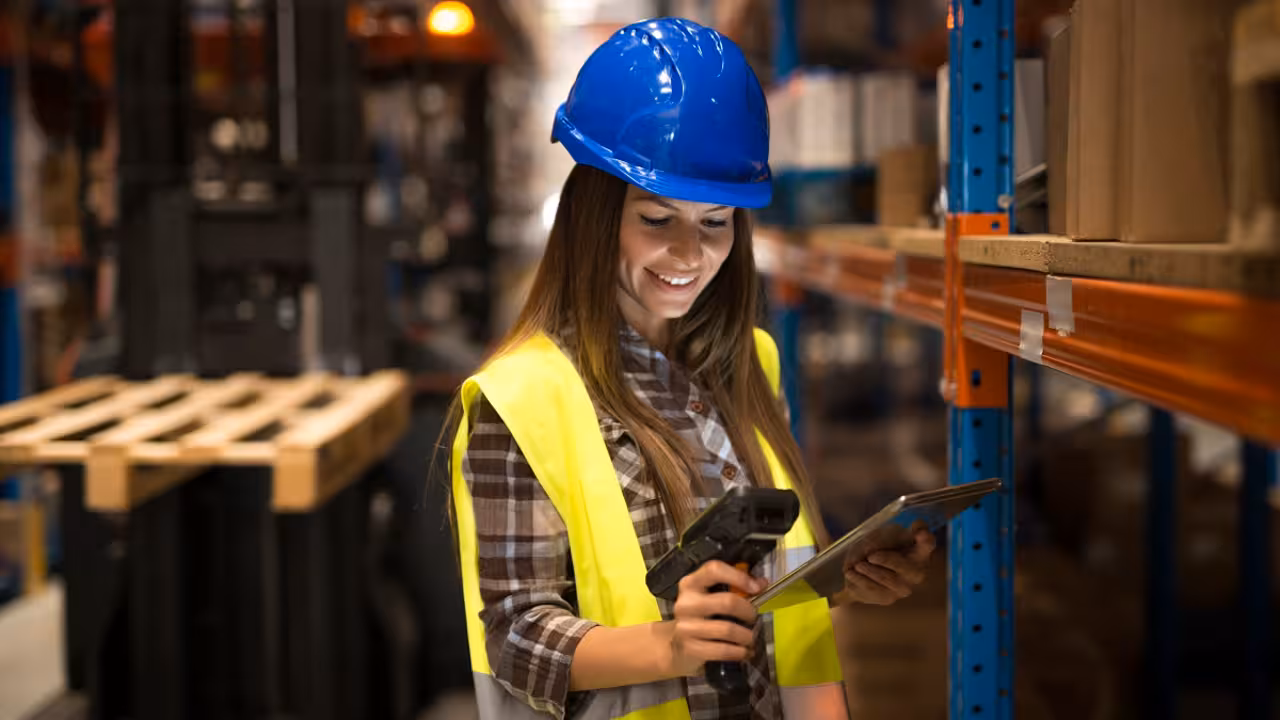 Smiling female worker holding tablet and bar code scanner checking inventory in distribution warehouse.
